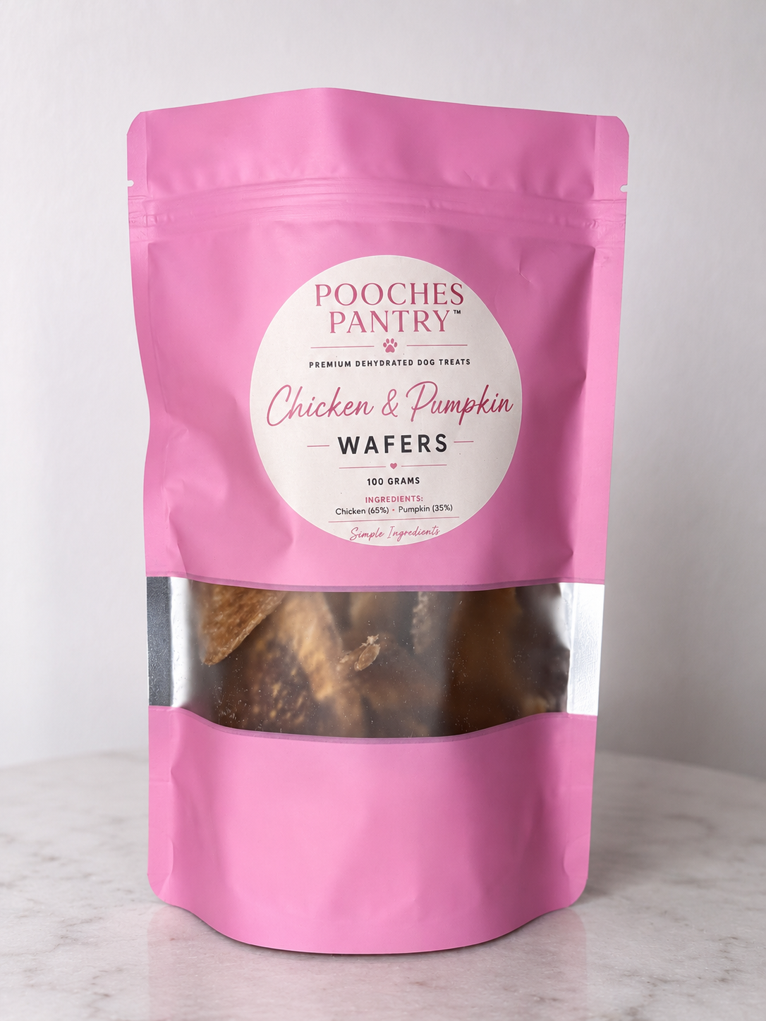 Chicken & Pumpkin Wafers dog treats in a pink Pooches Pantry bag on a marble bench