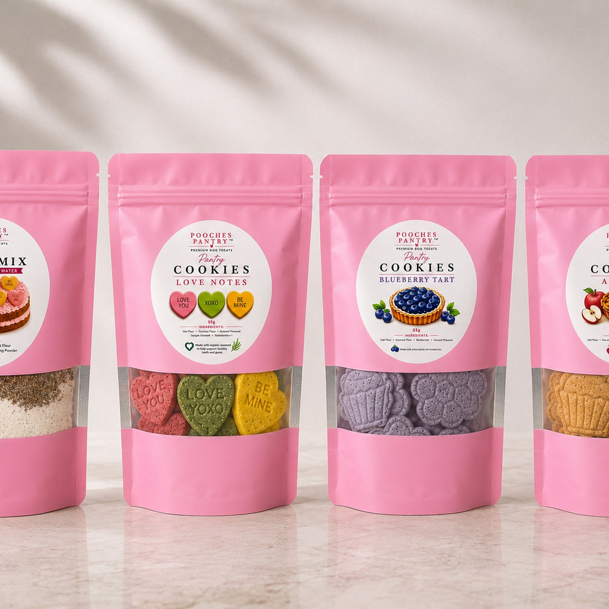 The Full Cookie Collection - four pink pouches of Pooches Pantry dog cookies lined up on a marble bench